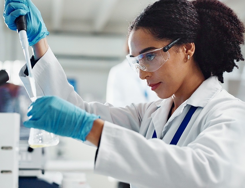 A researcher is holding a pipette and dropping liquid into a beaker.